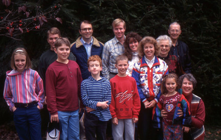 Mom (top right in red checkered top) in her element standing next to Dad and in company with a number of grandchildren, daughters-in-law, nephew and his wife, and grand-niece and grand-nephew.